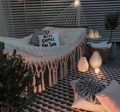 A hammock with tassels and printed cushions surrounded by lanterns and candles