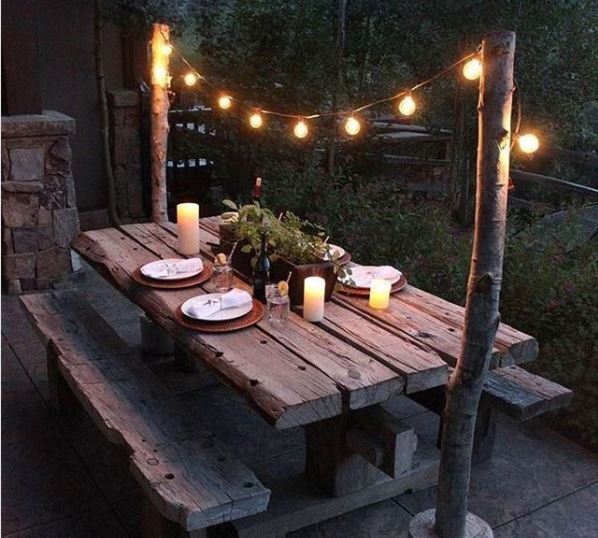 An old, weathered picnic table with place settings and string lights hanging above