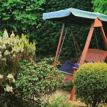 A traditional teak garden swing bench with canopy is tucked between hedges and shrubs