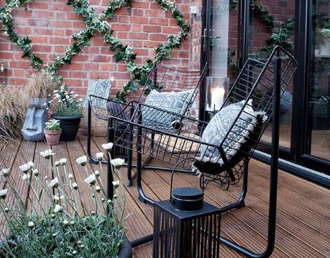 Two sleek wire chairs on a deck, surrounded by potted plants