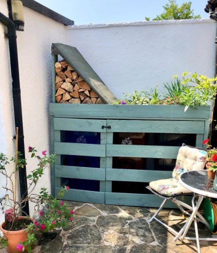 a DIY bin shelter with a small log store and green roof, and fits snugly in a garden nook.