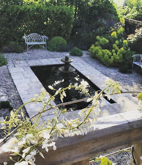 a rectangular pond with a fountain in the middle and white metal benches at the edge