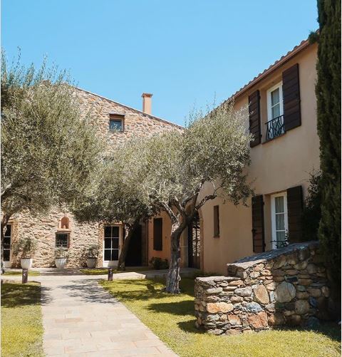 a sunny garden with olive trees, stone walls and a stone path leading throguh the centre