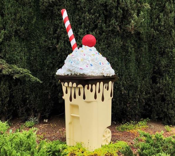 a wheelie bin that's been painted and accessorised to resemble an ice cream sundae with whipped cream and a cherry on the lid