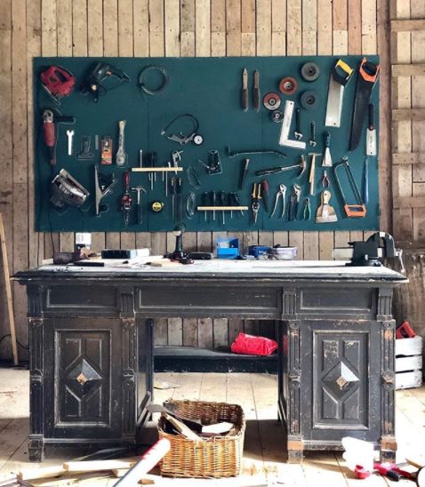 a worn antique desk used as a work bench, with an organised tool storage board on the wall behind