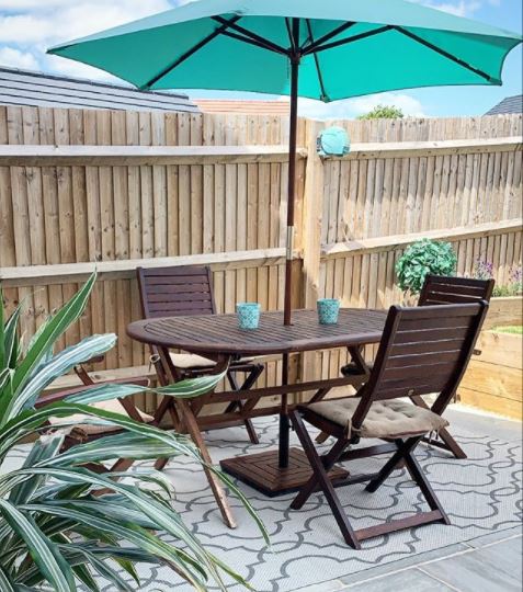 patio ideas using pale grey paving and an outdoor rug, beneath a wooden dining table and chairs