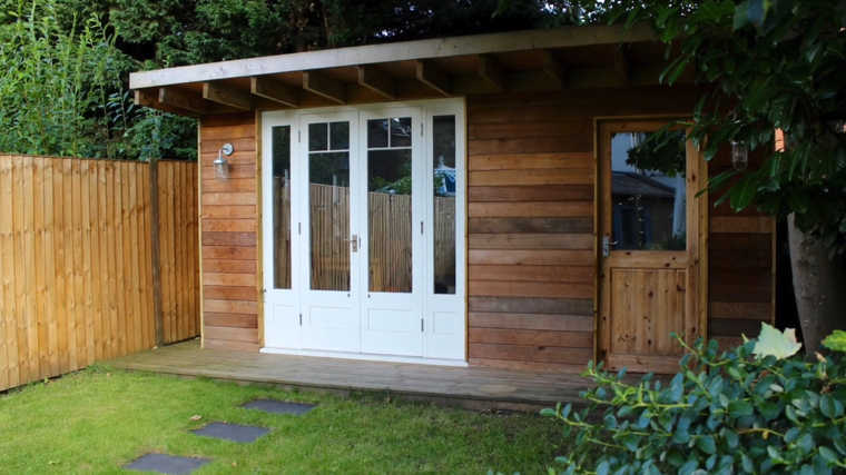 the exterior of a man cave shed with a deck at the end of a garden