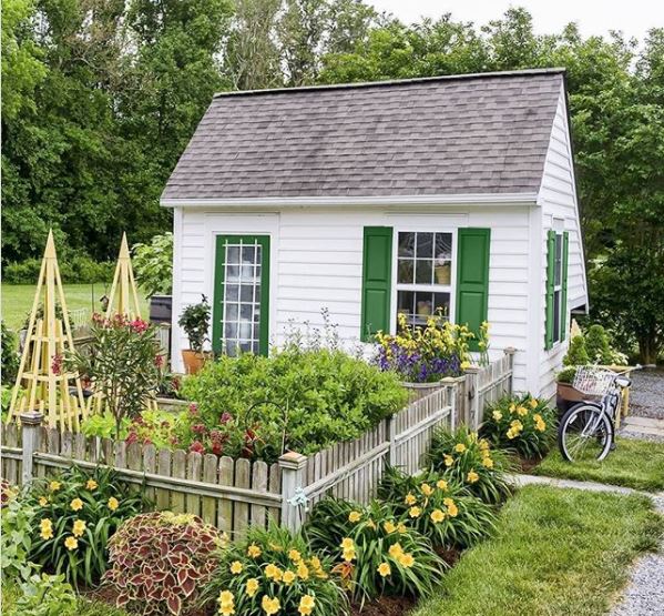 a white shed with green shutters around the windows and a green door