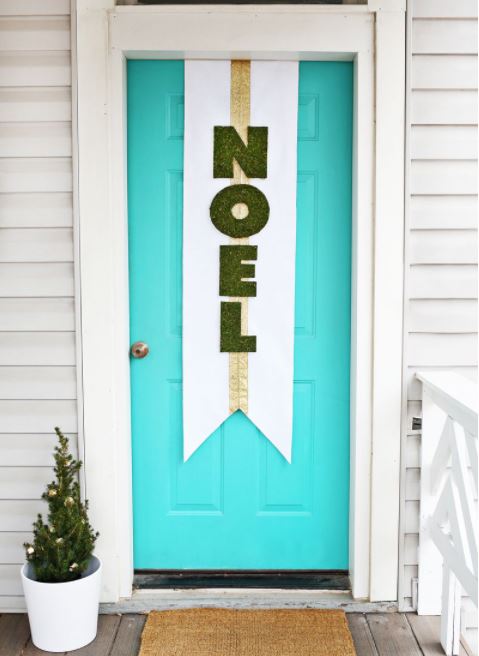 A bright blue door with a DIY "noel" sign hanging vertically