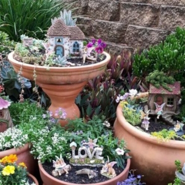 a garden with lots of pots, some of which have little fairy houses and decorations in